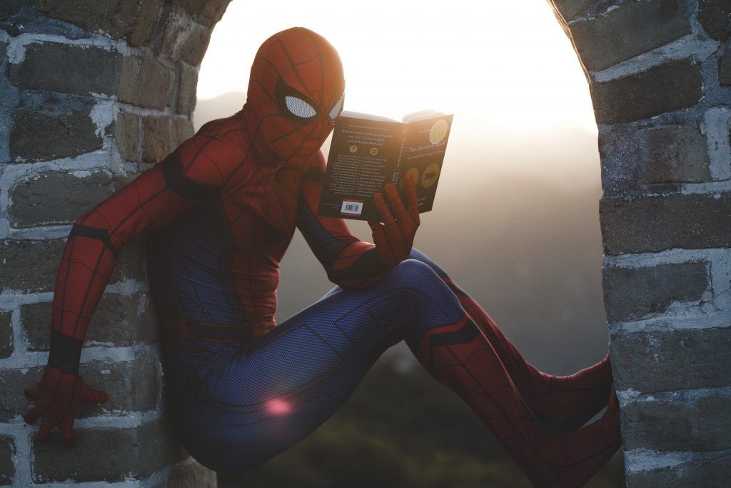 Illustration de Spider man qui lit un livre pour faire référence à la phase de conception des personnages, indispensable quand l'on créer une histoire. 